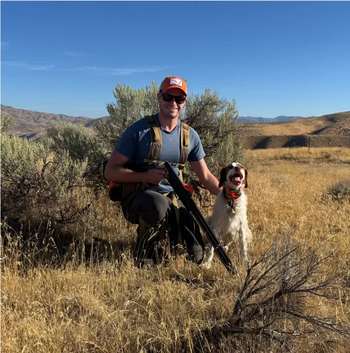Fisher kneeling with Chase, a Brittany, in the Idaho sagebrush hills